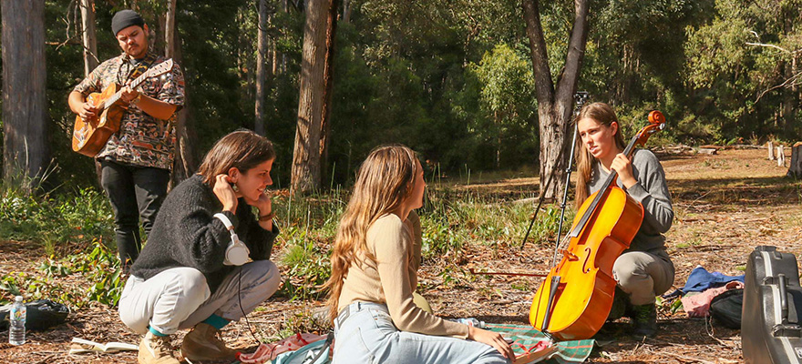 坐在森林里的地毯上听音乐家演奏乐器的学生
