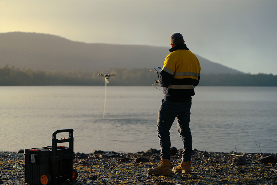 一个高可见度的人站在湖边，控制着一架无人机，从远处可以看到它正在从湖里采集水样
