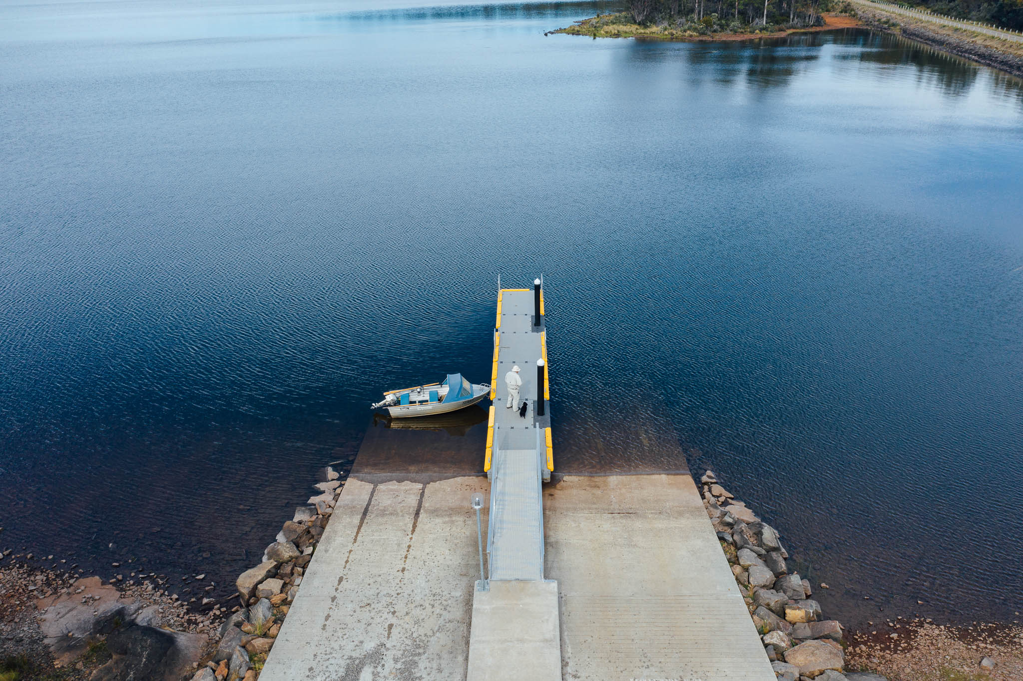 俯瞰勃朗特泻湖的船坡道，从海岸线延伸到清澈的蓝色泻湖。一个男人站在船坡道上，他的船系在左边。
