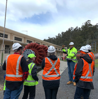 海德鲁塔斯公司的一名员工带领着一个发电站之旅，团队成员都戴着安全帽，神情严肃