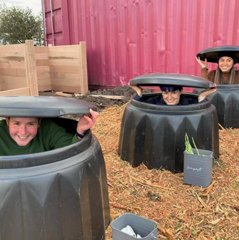 三个人坐在堆肥箱里对着镜头微笑