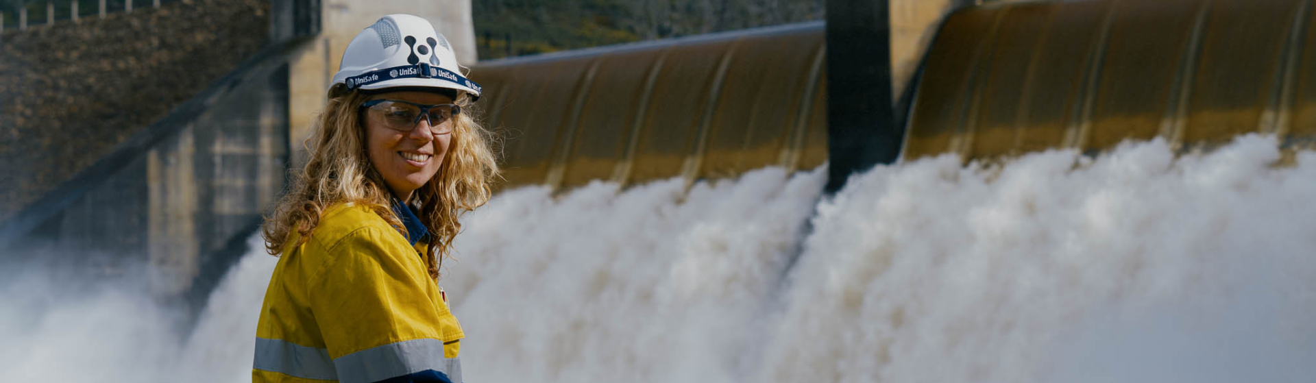 高姿态的人对着镜头微笑，站在一个溢出水的大坝前