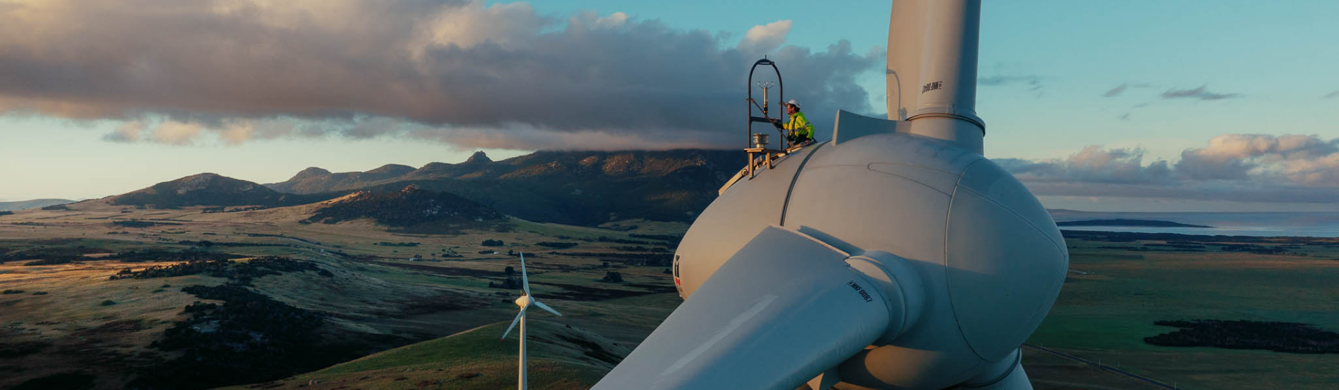 在国王岛，一名水力发电公司的员工在前景的风力涡轮机上工作，背景是另一台风力涡轮机