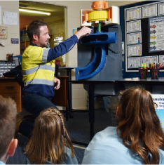一所小学的教室里，发电技术人员和学生们一起观看水电站如何运行